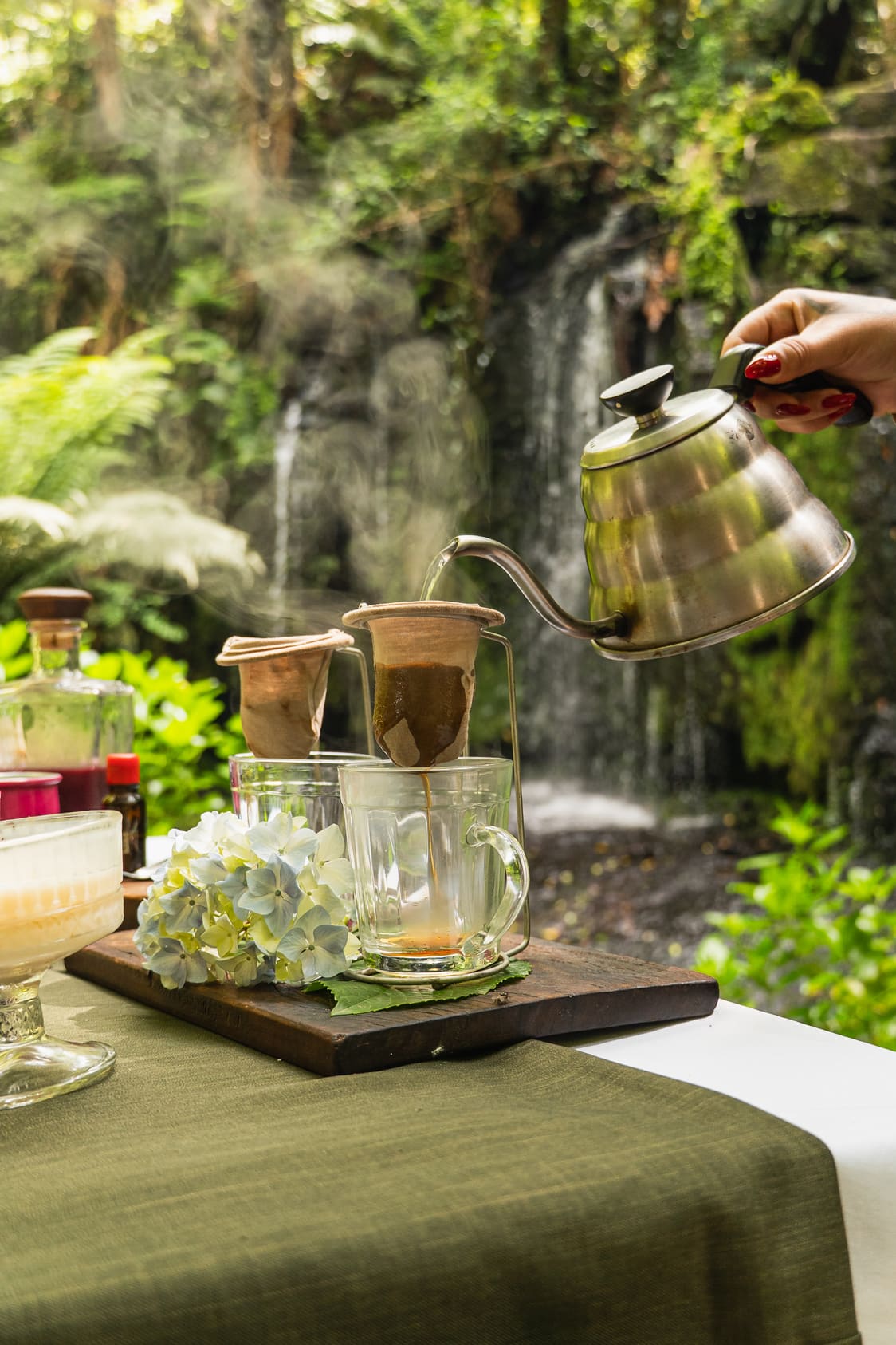 Café sendo passado na mesa posta diante da cachoeira
